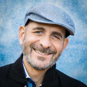 a smiling man wearing a hat and a black jacket